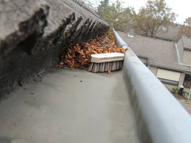 Dakgoot gevuld met herfstbladeren en een borstel, gereed voor professionele reiniging